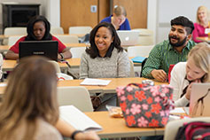 Group of people sitting at tables with notes and laptops. Link to Gifts by Estate Notes.